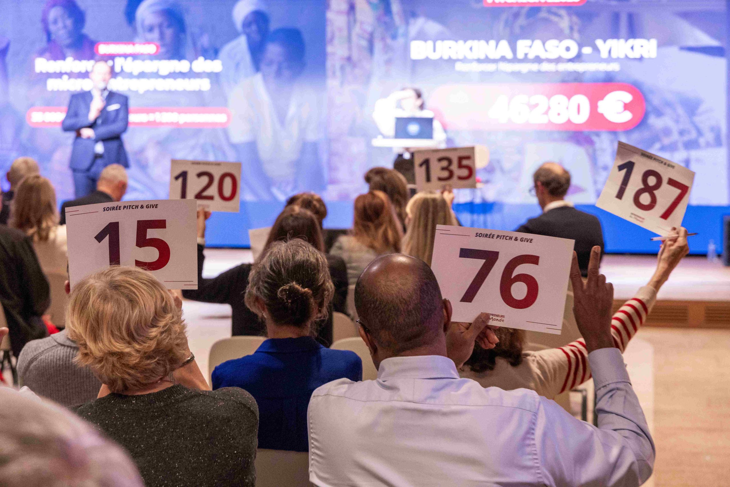Participants au Pitch&Give 2025 de dos, tenant des pancartes numérotées